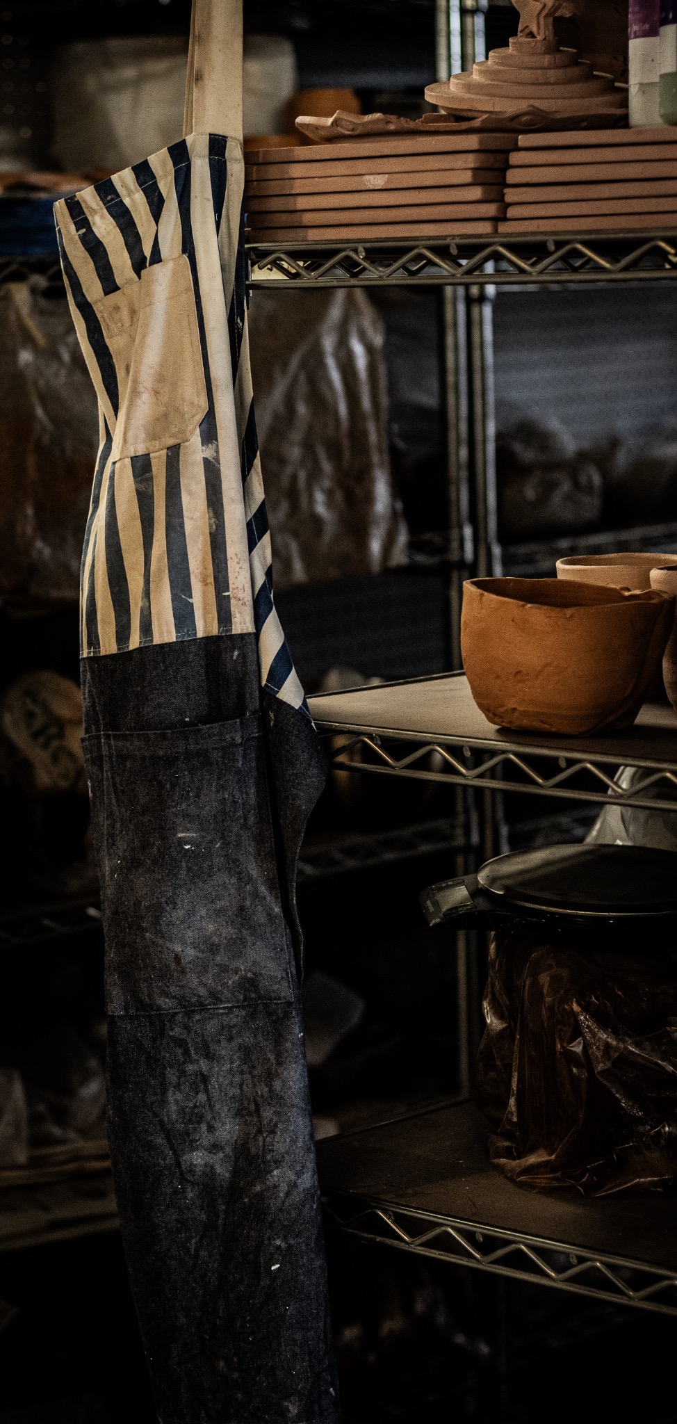 A clay-stained apron hanging among studio shelves and unfinished pottery