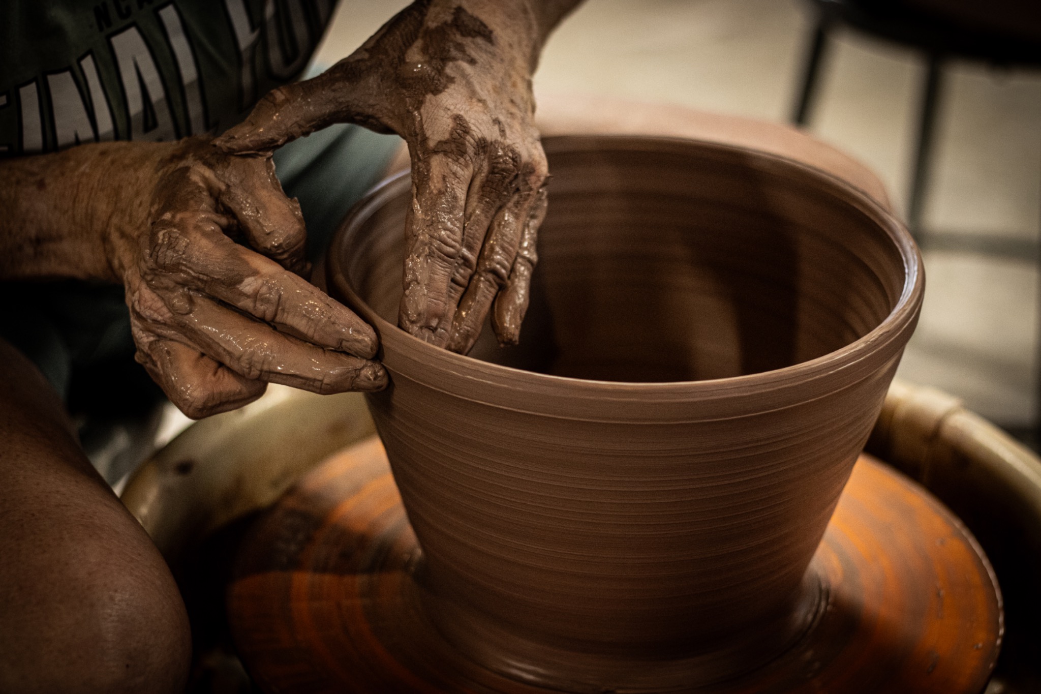 Clay-covered hands shaping a vessel on a pottery wheel