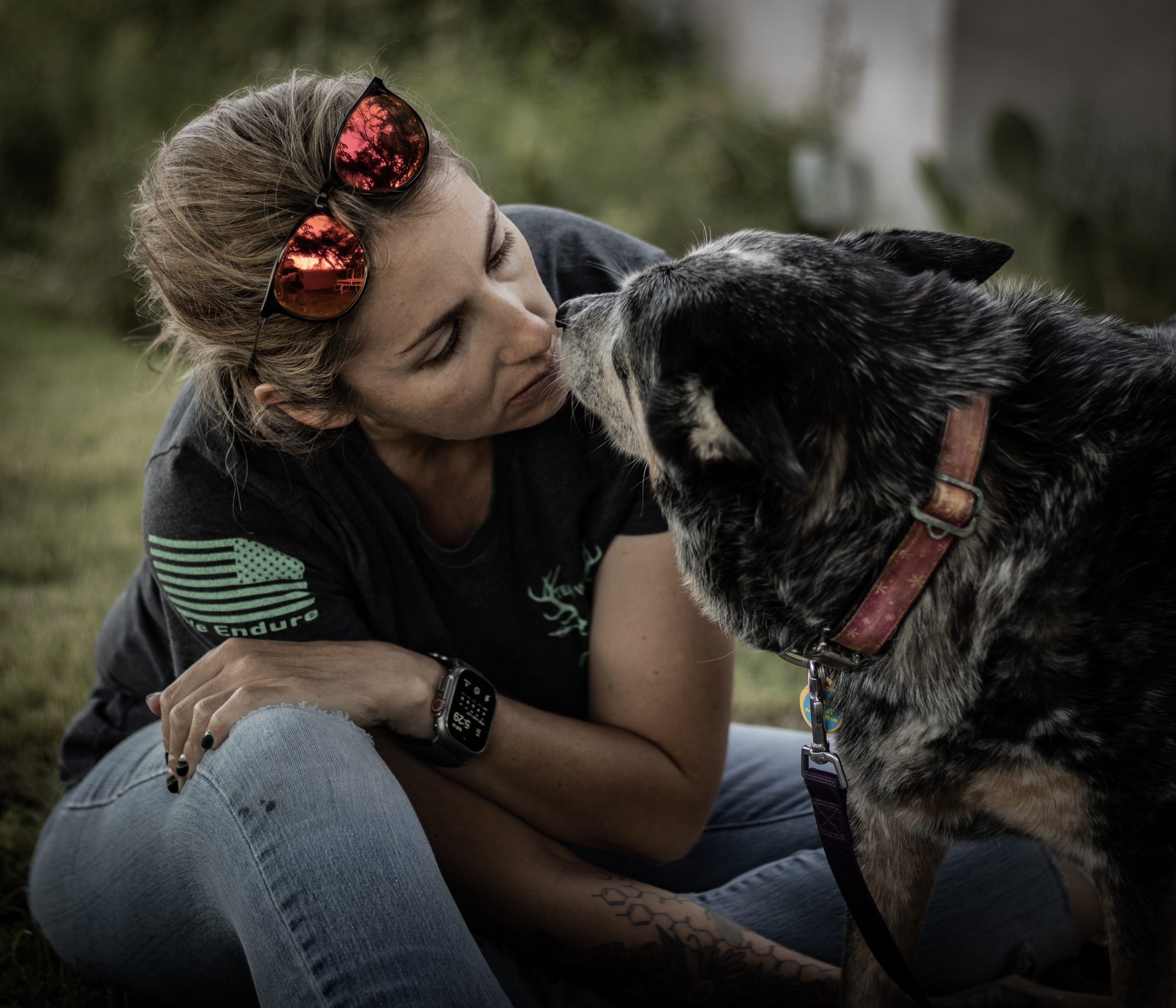 A woman and a speckled dog lean toward each other with their noses nearly touching