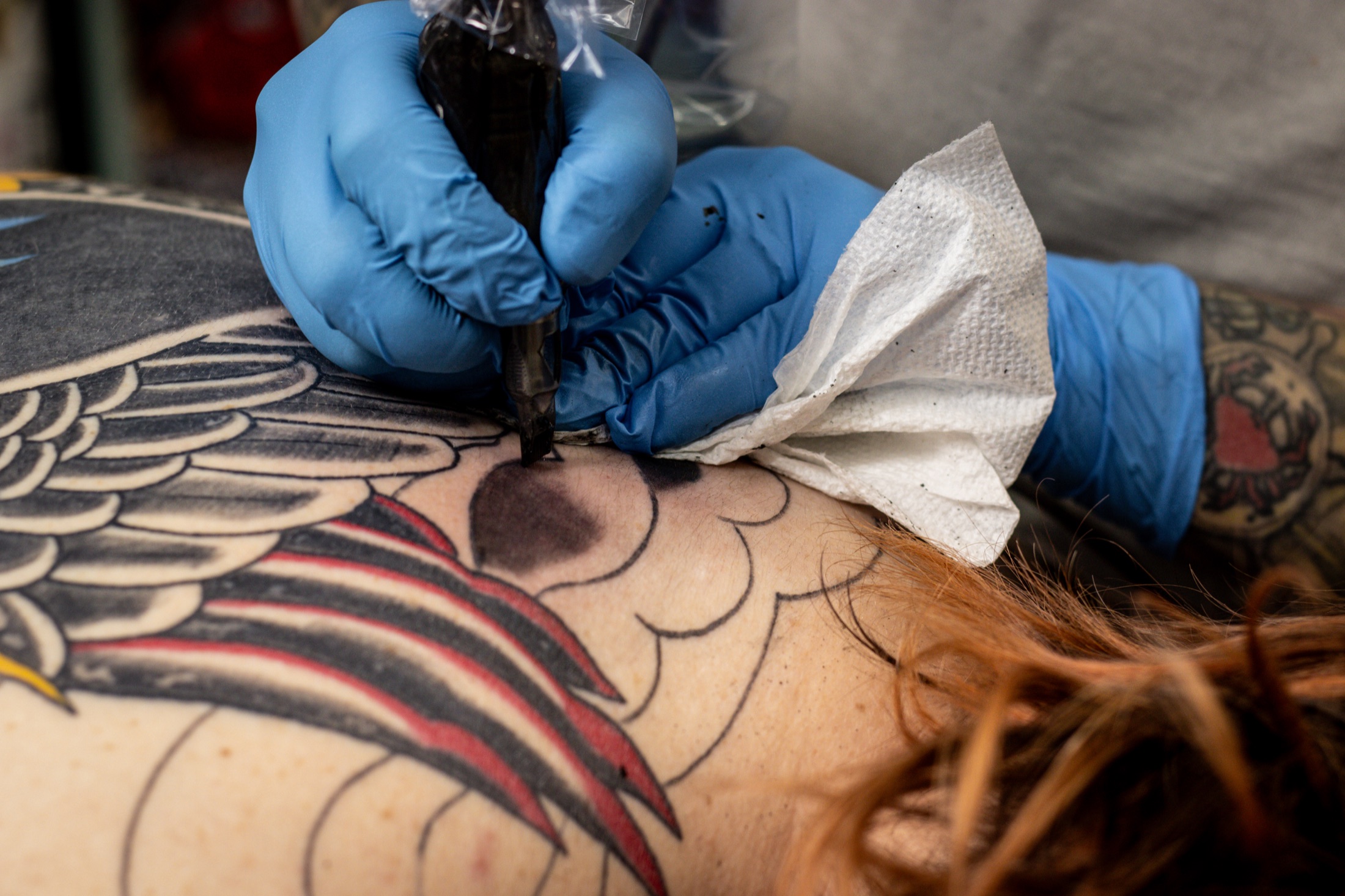 Gloved hands guiding a tattoo machine across a client’s skin